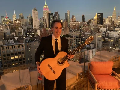omas Rodriguez performing solo guitar at a rooftop event with the Manhattan skyline behind him.