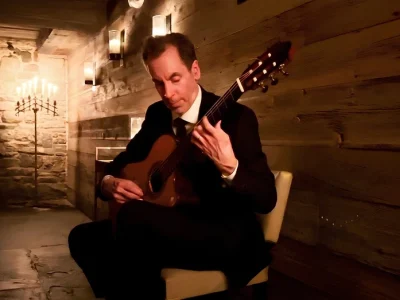 Tomas Rodriguez playing classical guitar in a candlelit stone wine cellar at a private event in New York.